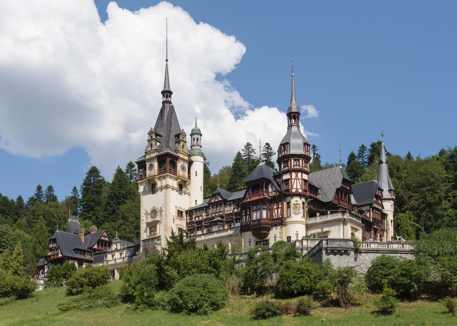 The towers and half-timbered facades of Peleș Castle among fir trees in Sinaia