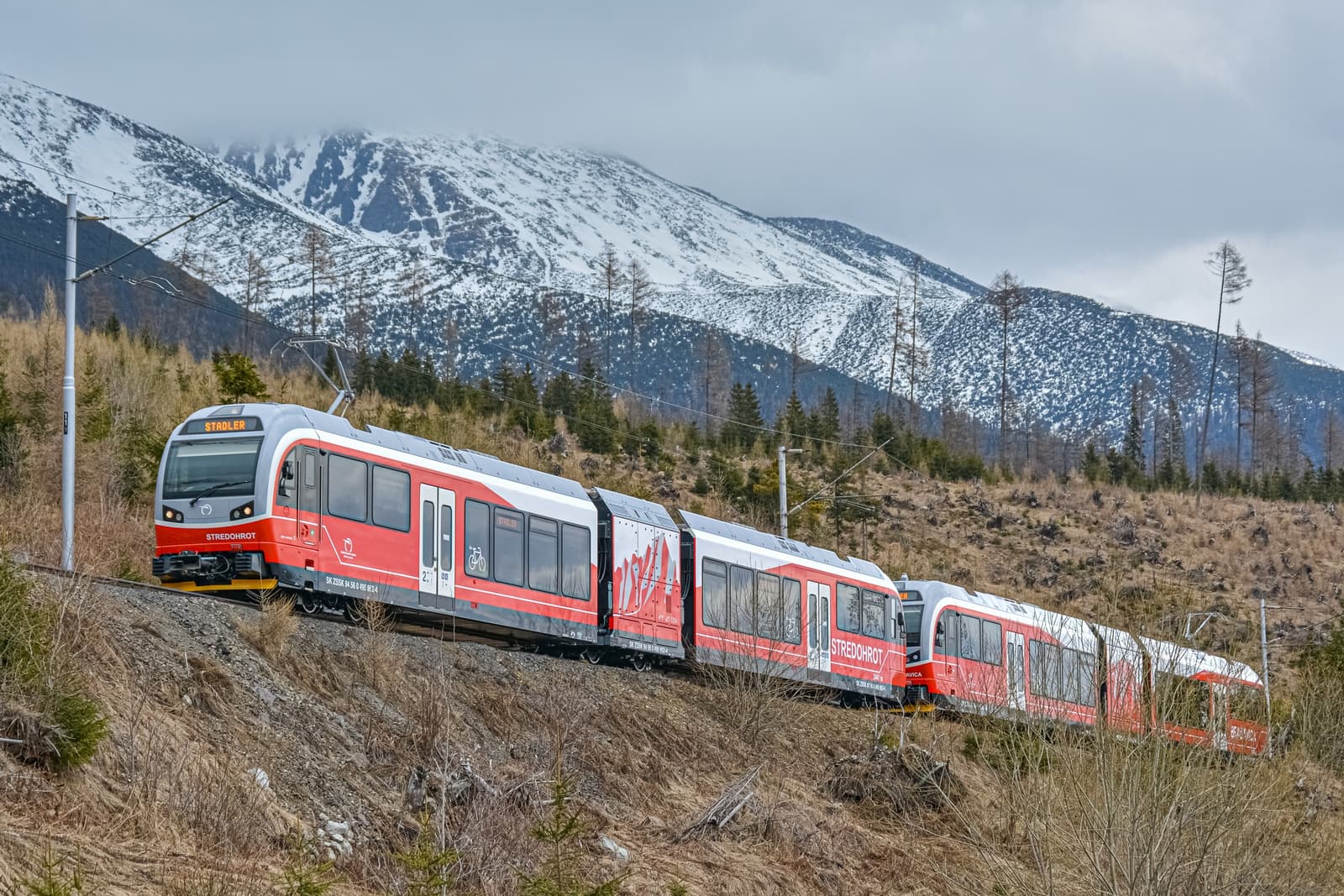 A red Tatra Electric Railway train below the snowy High Tatras
